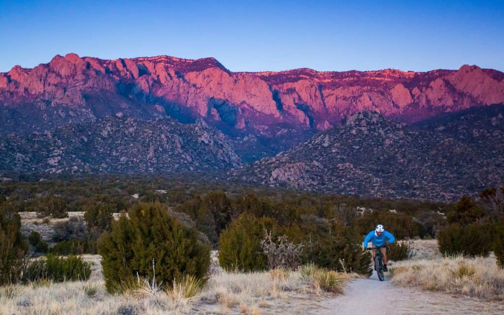 mountain biking man pedals through the desert mountain landscape as the sunset hits the mountains. such beautiful nature scenery and outdoor sports and recreation can be found when visiting new mexico, the land of enchantment. horizontal composition. sandia mountains. albuquerque, new mexico.