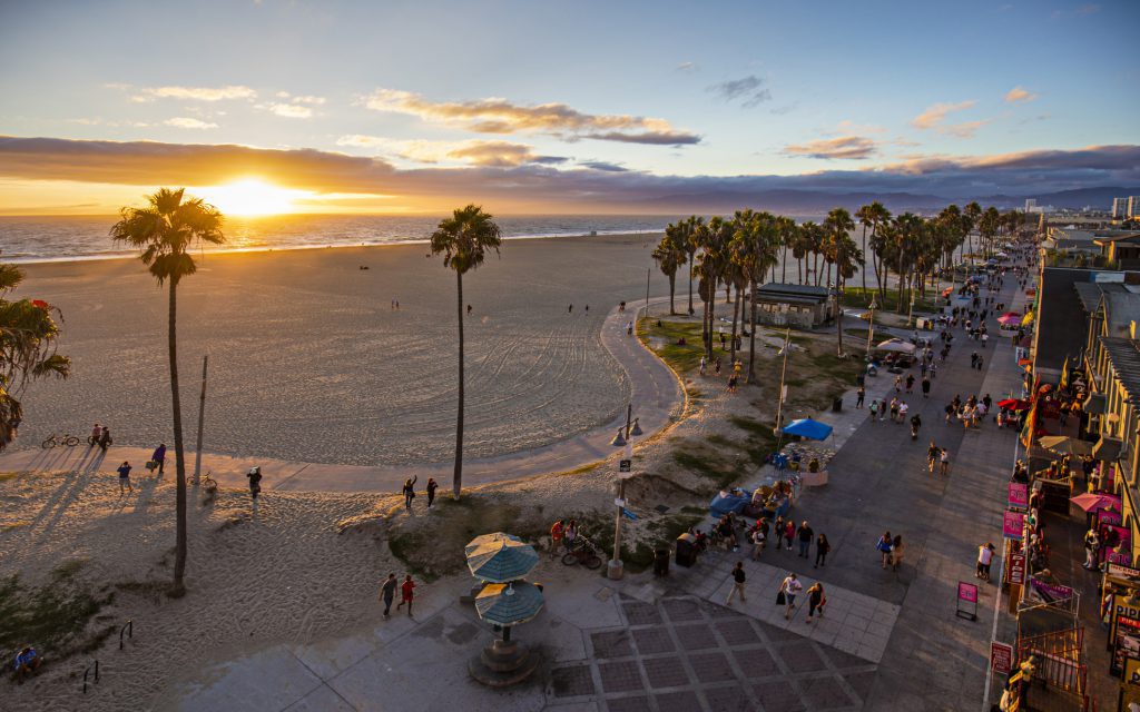 Tourists walking on footpath by Venice beach during sunset